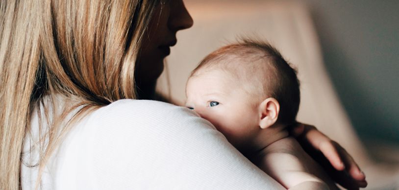 Close up of newborn baby peeking over the shoulder of a woman holding them