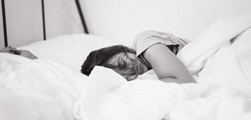 black and white photo of a woman sleeping under a white quilt