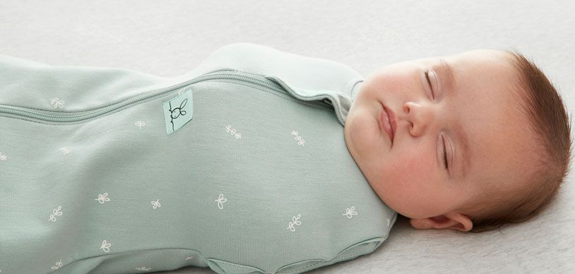 Newborn sleeping in crib, wearing the ergoPouch Cocoon Swaddle Sack in Sage