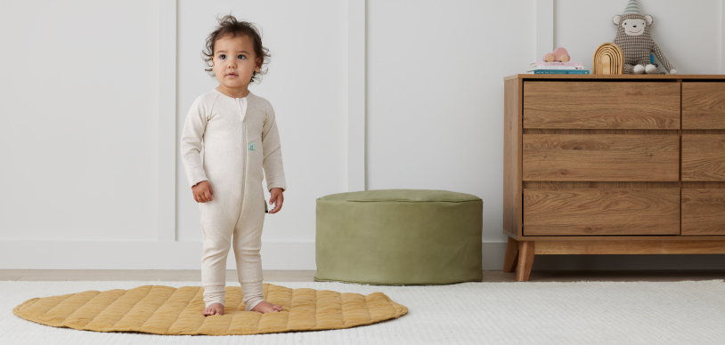 Cute toddler wearing oatmeal marle romper standing in the nursery 