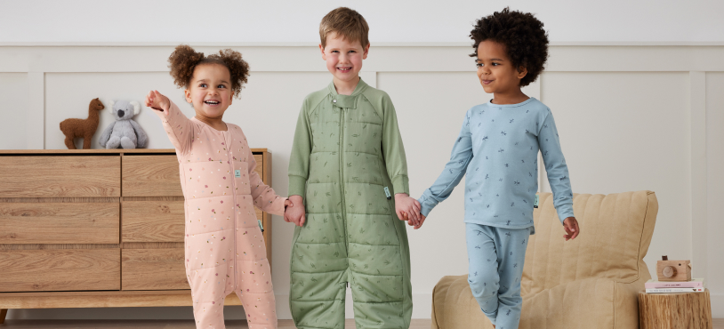 3 preschoolers holding hands wearing sleep sacks and onesies