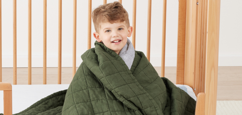 Toddler boy snuggling in big bed with green ergoPouch bedding