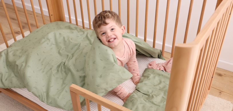 toddler sitting in bed wrapped in blanket wearing pajamas