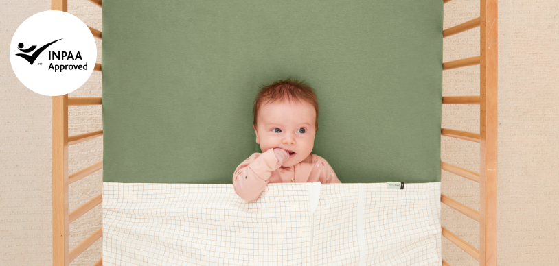 Baby being tucked into bassinet under ergoPouch zip-up Baby Tuck Sheet